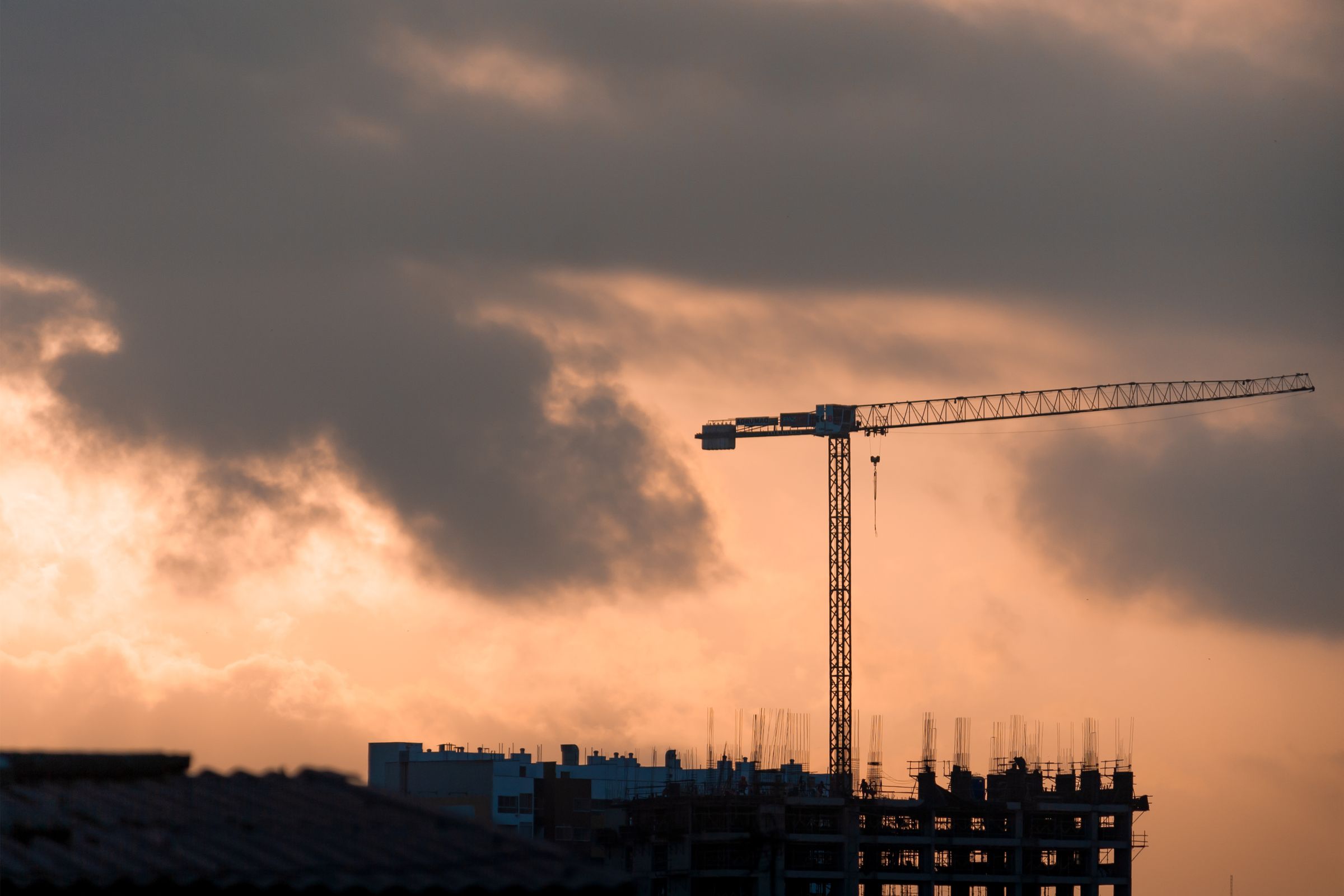 Tower crane and building frame silhouetted against sunset cloud