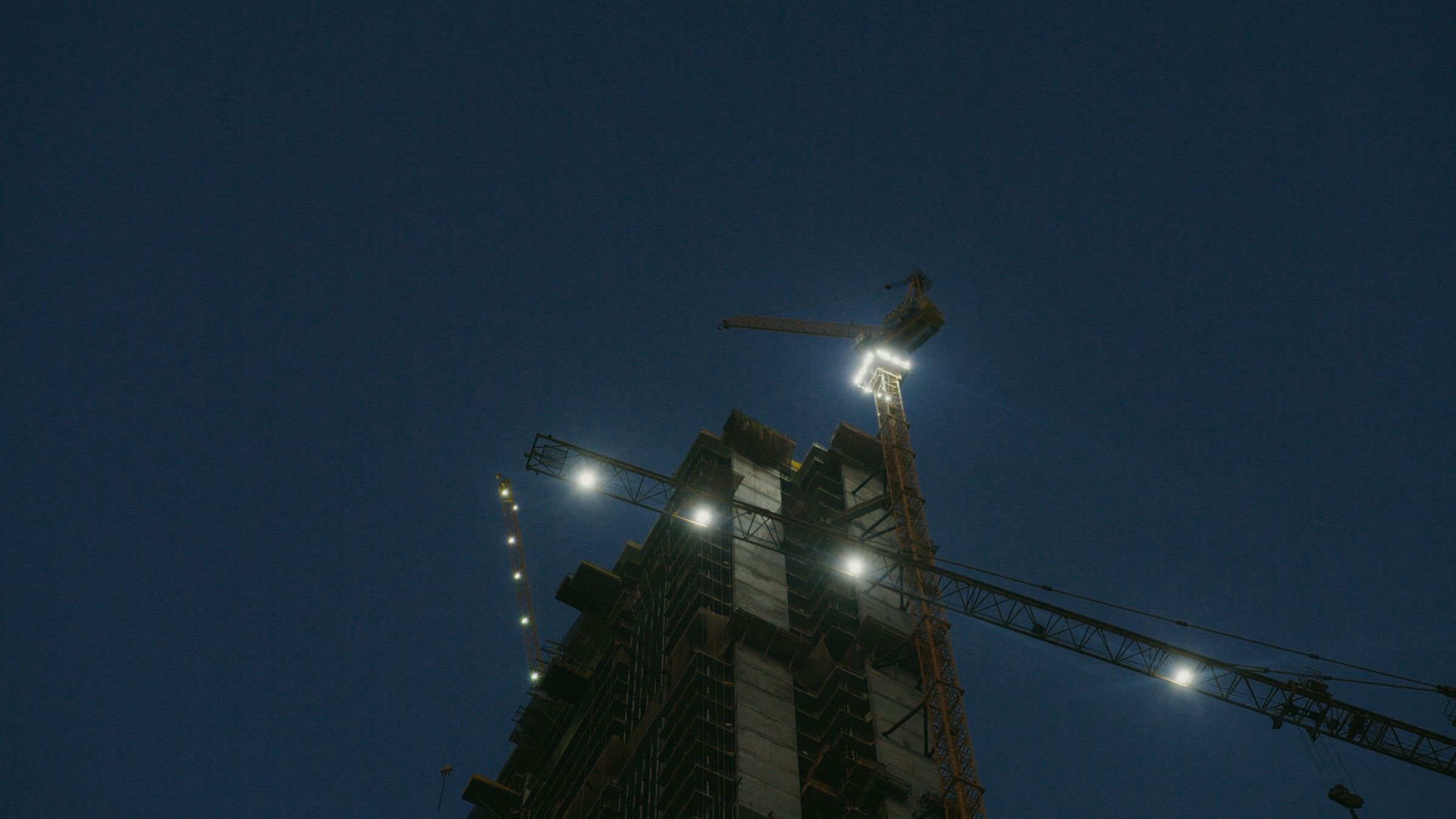 Building frame and crane lit against a deep blue night sky